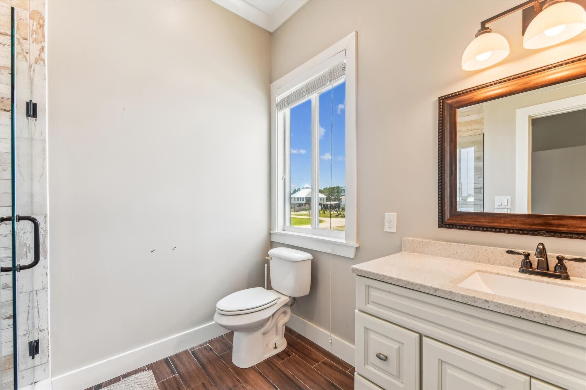 A bathroom with a toilet, a vanity with a mirror, and a window with a view of the outside.