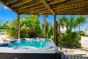 Un jacuzzi bajo una pérgola de madera, con palmeras y un cielo despejado al fondo.