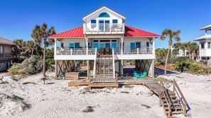 A two-story beach house with a red roof, a balcony, and a wooden deck leading to the beach. - Welcome to DUNE IT RIGHT! (St. George Island)