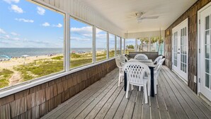 A covered porch with a view of the beach, a table with chairs, and a ceiling fan. - Wander from the cool shade of the screened porch to the sun deck with your favorite book! (St. George Island)