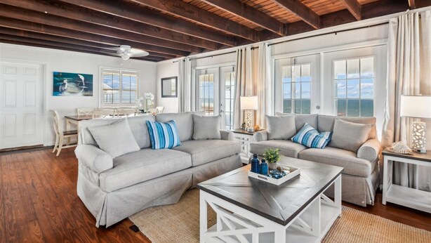 A spacious living room with a wooden ceiling, a grey sofa set, a coffee table, and a dining area with a table and chairs. - Wander from the cool shade of the screened porch to the sun deck with your favorite book! (St. George Island)