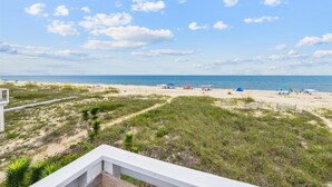 A beach view with a clear sky, sandy beach, and some vegetation. - Wander from the cool shade of the screened porch to the sun deck with your favorite book! (St. George Island)