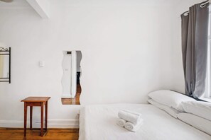 A room with a bed, a small wooden table, a mirror, and a window with curtains.