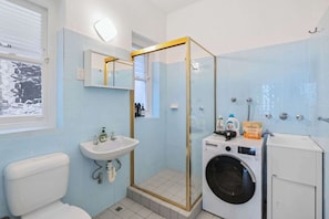 A bathroom with a toilet, sink, glass shower enclosure, washing machine, and a mirror.