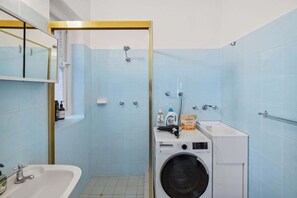 A bathroom with a sink, mirror, shower, and a washing machine.