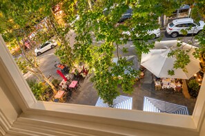 An outdoor dining area with tables and umbrellas, surrounded by trees and a street view.