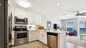 A modern kitchen with stainless steel appliances, white cabinetry, and a large island. - Welcome to Ocean Mile H-8! (St. George Island)