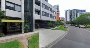 A modern building with a glass entrance, a parking area, and a street with cars.