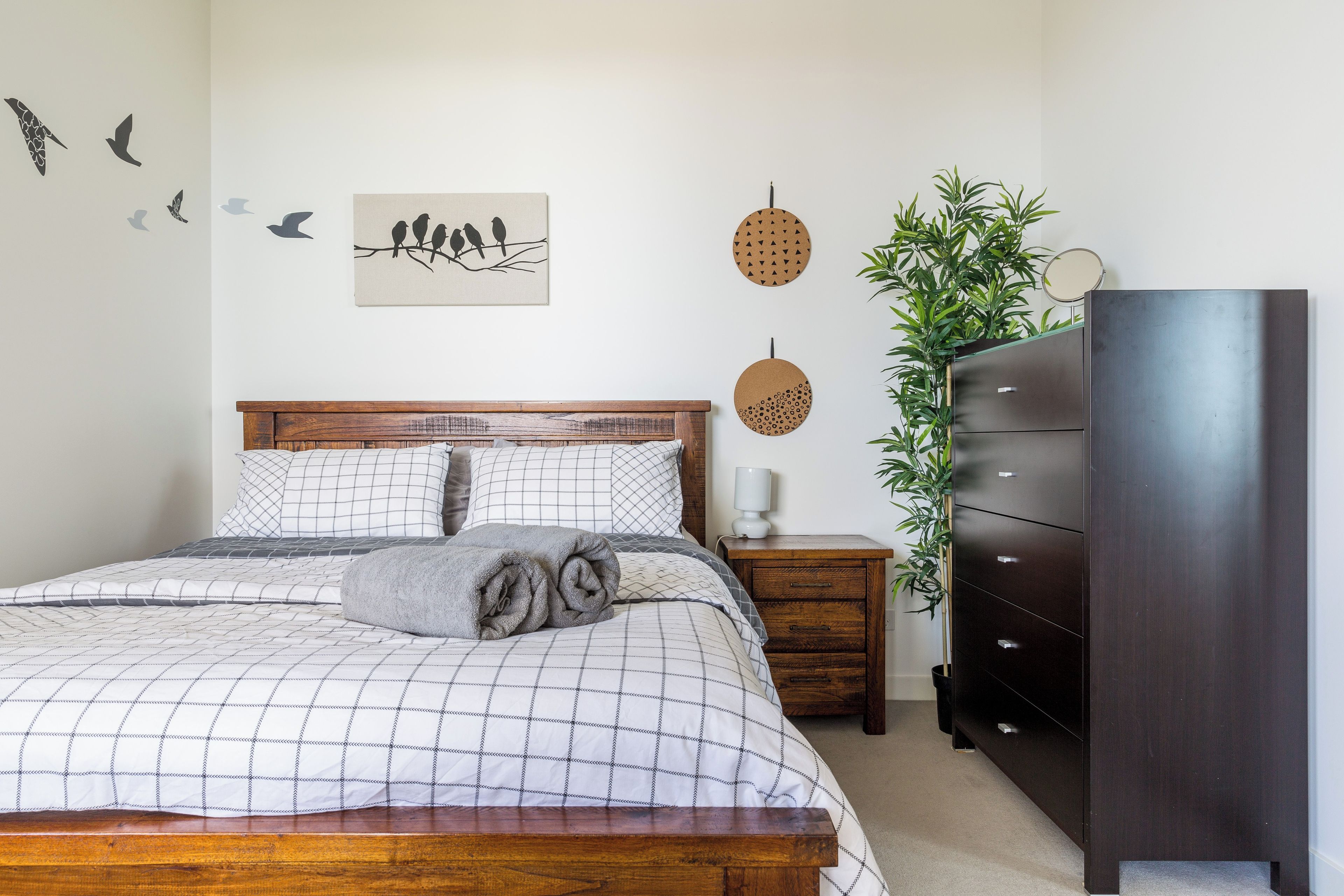 Une chambre à coucher avec un lit en bois, une table de chevet, une commode et des éléments de décoration murale comprenant des motifs d’oiseaux et des formes circulaires.