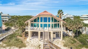 A beachfront house with a balcony, a staircase leading to the entrance, and a sandy beach in the foreground. - Welcome to Island Dream, where dreams come true! (St. George Island)