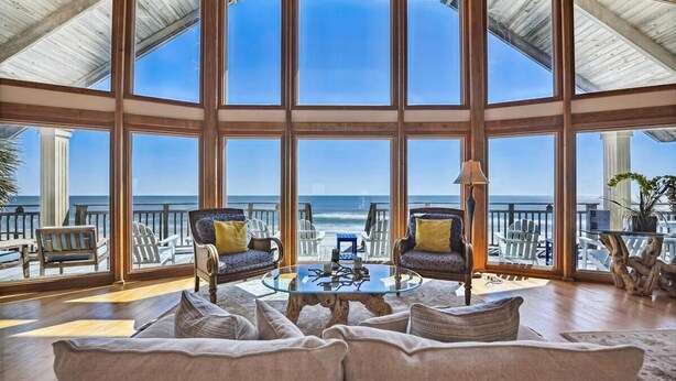 A spacious room with a large glass wall offering a view of the ocean. There are two sofas and a coffee table in the center. - Welcome to Island Dream, where dreams come true! (St. George Island)