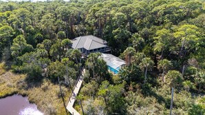 Ein Haus, umgeben von dichtem Wald, mit freiem Blick auf ein Schwimmbad und eine Holzterrasse, die zum Haus führt.