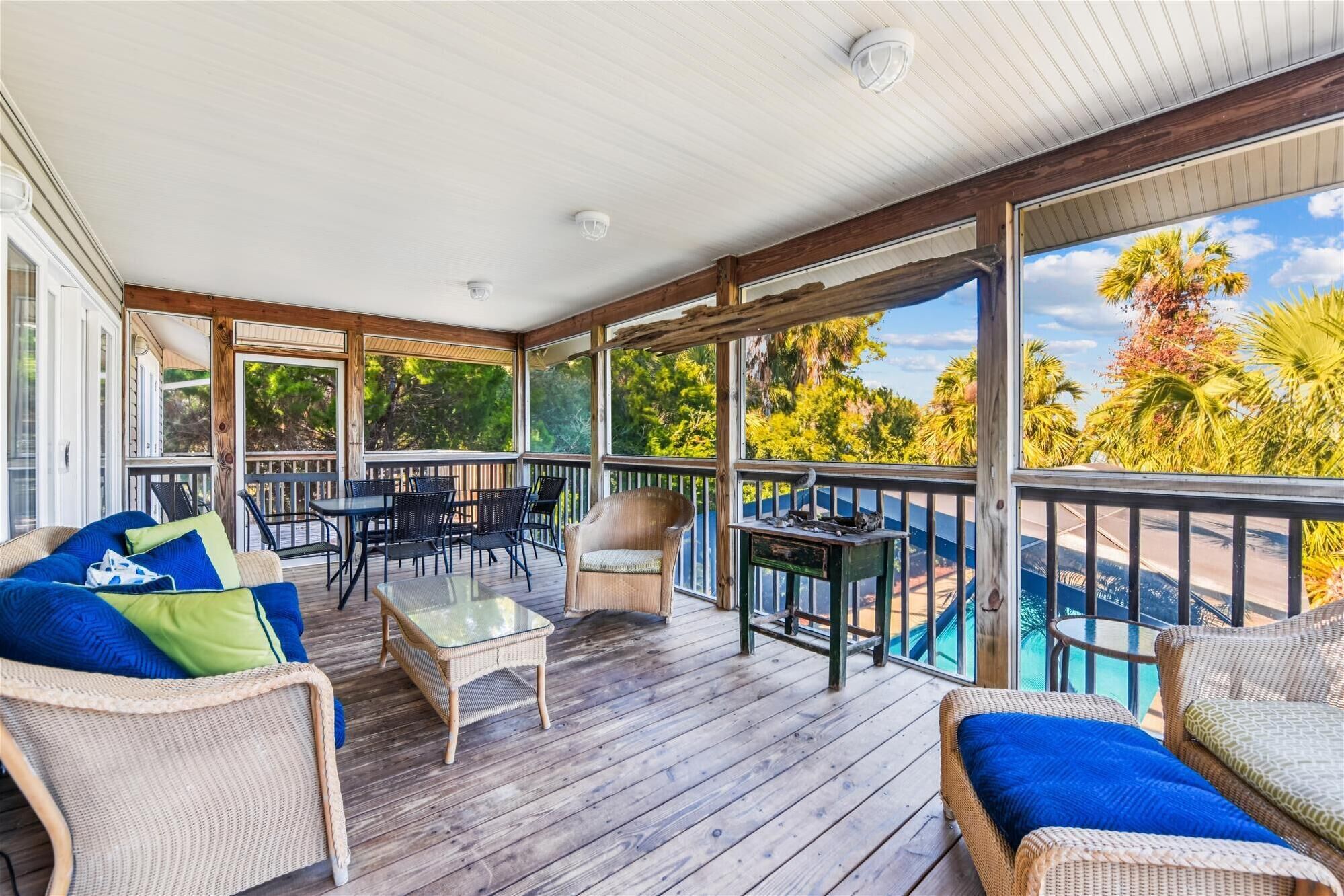Eine überdachte Terrasse im Freien mit Korbmöbeln, einem Glastisch und Blick auf einen Swimmingpool.