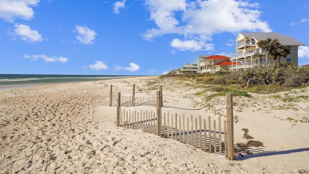 Ein Anwesen direkt am Strand, mit Holzlattenzaun, Strand und einem Gebäude mit mehreren Balkonen und rotem Dach.