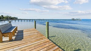 Eine Holzsteg, der sich in klares, blaues Wasser erstreckt, mit einer Bank und einem entfernten Steggebäude.