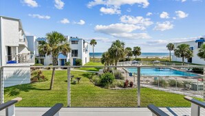 A pool area with a view of the beach, surrounded by palm trees and modern buildings. - Welcome to Villa E-5! (St. George Island)