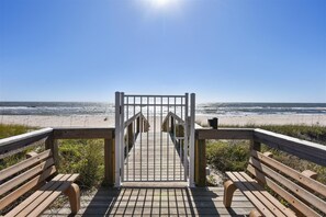 A wooden boardwalk leading to a beach with a gate in the center.
