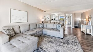 A modern living room with a sectional sofa, a dining area, and a kitchen in the background. - Welcome to Villa E-5! (St. George Island)