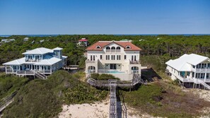 Une vaste propriété située en bord de mer, comprenant plusieurs maisons, un bâtiment principal avec un toit rouge et une promenade en bois menant à la plage.