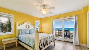 Een slaapkamer met een bed, nachtkastje, plafondventilator en uitzicht op het strand door een schuifdeur.