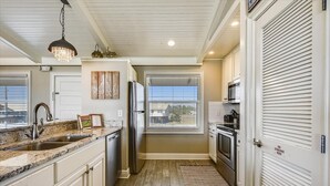 Una cocina con gabinetes blancos, encimera de granito, refrigerador de acero inoxidable y microondas.