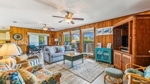 A cozy living room with wooden walls, a ceiling fan, a sofa, a coffee table, and a television. - Welcome to Brief Escape! (St. George Island)
