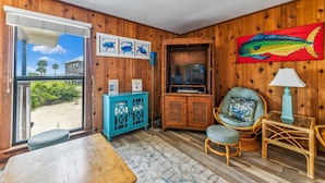 A wooden interior with a view of the beach, a television, wicker furniture, and a colorful fish painting. - Welcome to Brief Escape! (St. George Island)