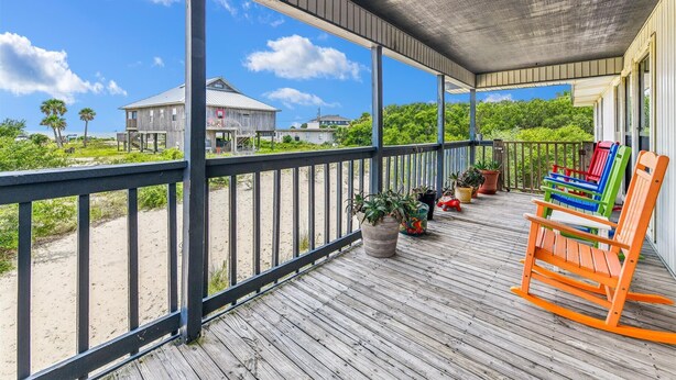 A wooden deck with a railing, potted plants, and colorful chairs. - Welcome to Brief Escape! (St. George Island)