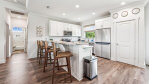 A modern kitchen with white cabinets, a stainless steel refrigerator, and a central island with bar stools. - Welcome to Anchors Up! (St. George Island)