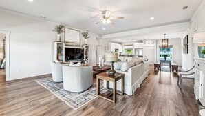 A spacious living room with a large TV, comfortable seating, a dining area, and a kitchen in the background. - Welcome to Anchors Up! (St. George Island)