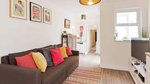 A living room with a brown sofa, colorful cushions, a patterned rug, and framed artwork on the wall. - Charming Riverside Apartment Minutes from City (Dublin)