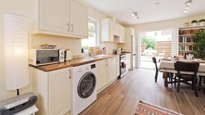 A modern kitchen with white cabinets, a washing machine, a microwave, and a dining area with a table and chairs. - Charming Riverside Apartment Minutes from City (Dublin)