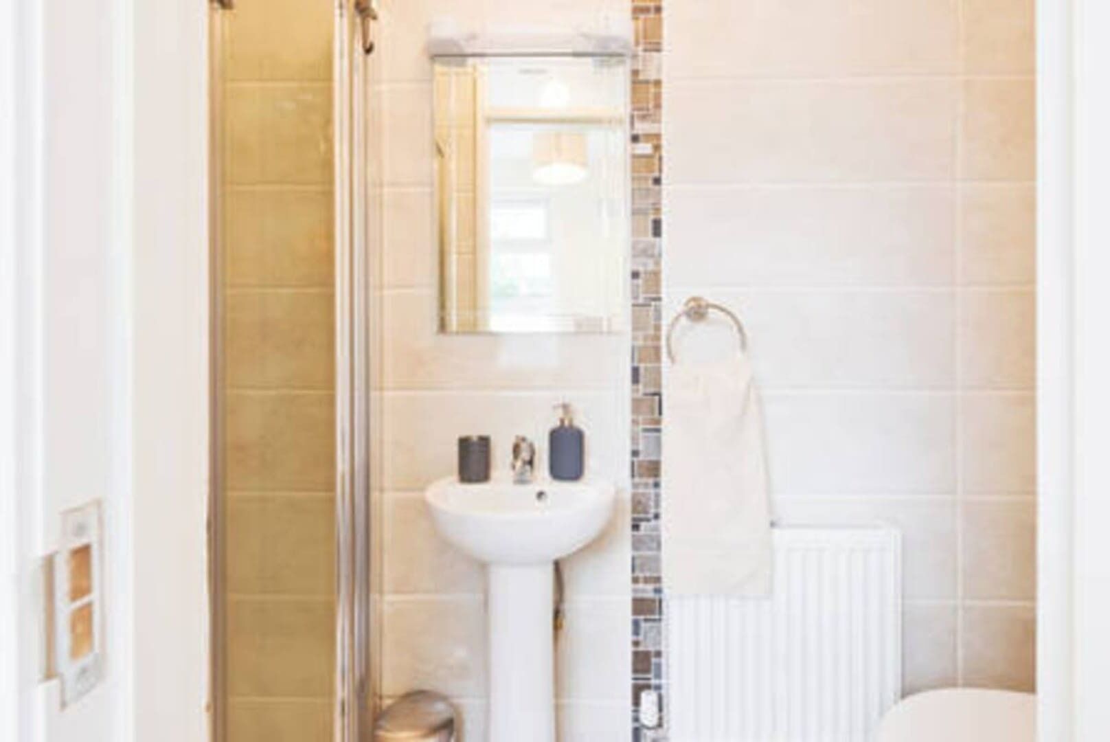 A bathroom with a glass shower enclosure, a white sink, and a towel rack.