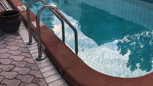 Una piscina con barandillas de metal, cerca blanca y una planta en maceta.