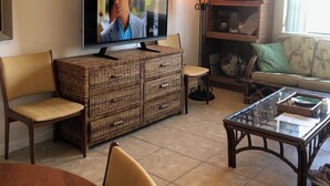 Una sala de estar con televisor, muebles de mimbre, una mesa de centro de vidrio y un sofá.