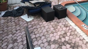 Zona junto a la piscina con una valla blanca, un sofá de mimbre, dos taburetes negros y una piscina con la marca de profundidad 3 pies.