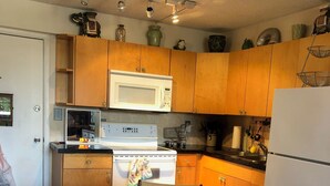 Una cocina con gabinetes de madera, un refrigerador blanco, un microondas y una estufa. Hay una mesa de comedor con una silla frente a ella.