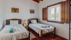 Una habitación con dos camas de madera, una ventana con contraventanas de madera y una mesita de noche con una lámpara.