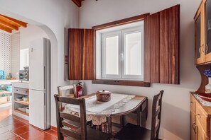 Une cuisine équipée d’une table à manger, de chaises, d’un réfrigérateur et d’une fenêtre avec des volets en bois.