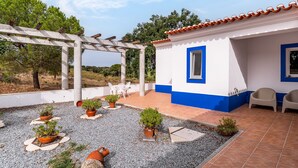 Un patio cubierto con plantas en macetas, mobiliario exterior y una pérgola blanca.