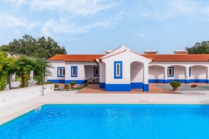 Un bâtiment doté d’une piscine, avec une façade bleue et blanche et un toit recouvert de tuiles rouges.