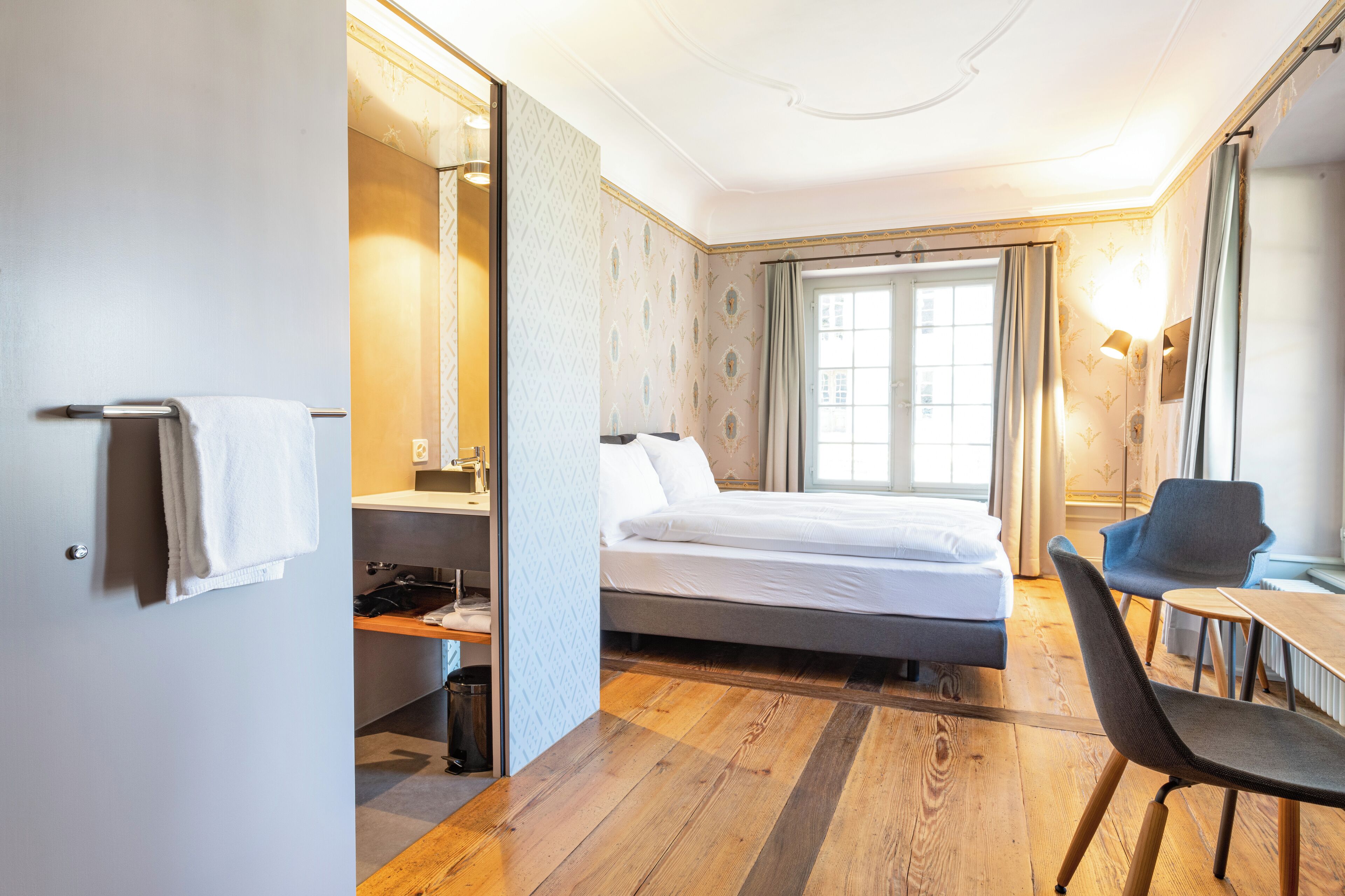 Une chambre d’hôtel avec un lit, un bureau, une chaise, un miroir et une fenêtre.