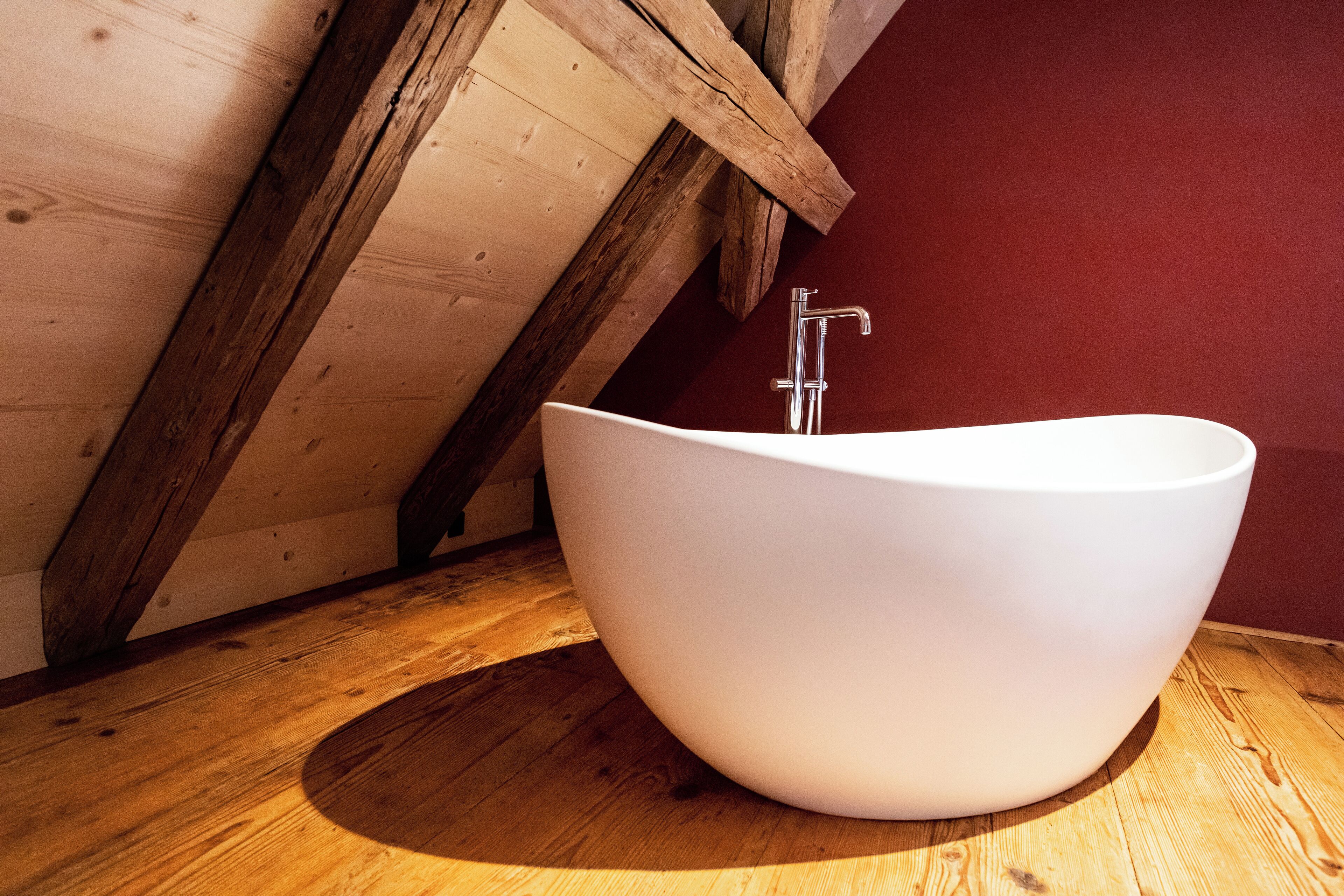 Une baignoire blanche, autoportante, se trouve dans une pièce en bois dont le plafond est incliné.