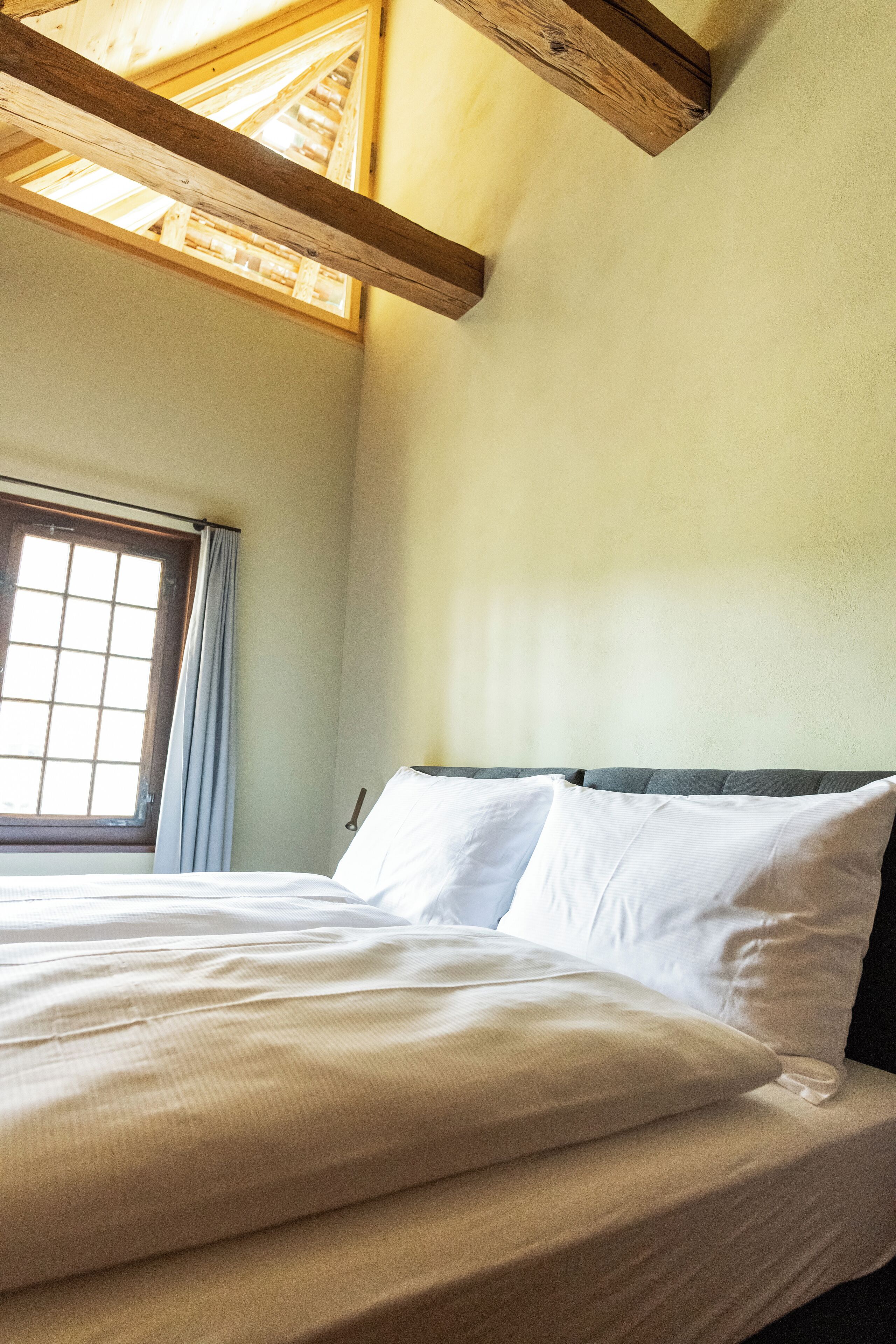 Quarto com cama, janela e vigas de madeira no teto.