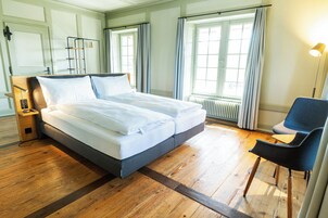 Una cama doble con cabecera de madera, una mesita de noche con lámpara y una silla.