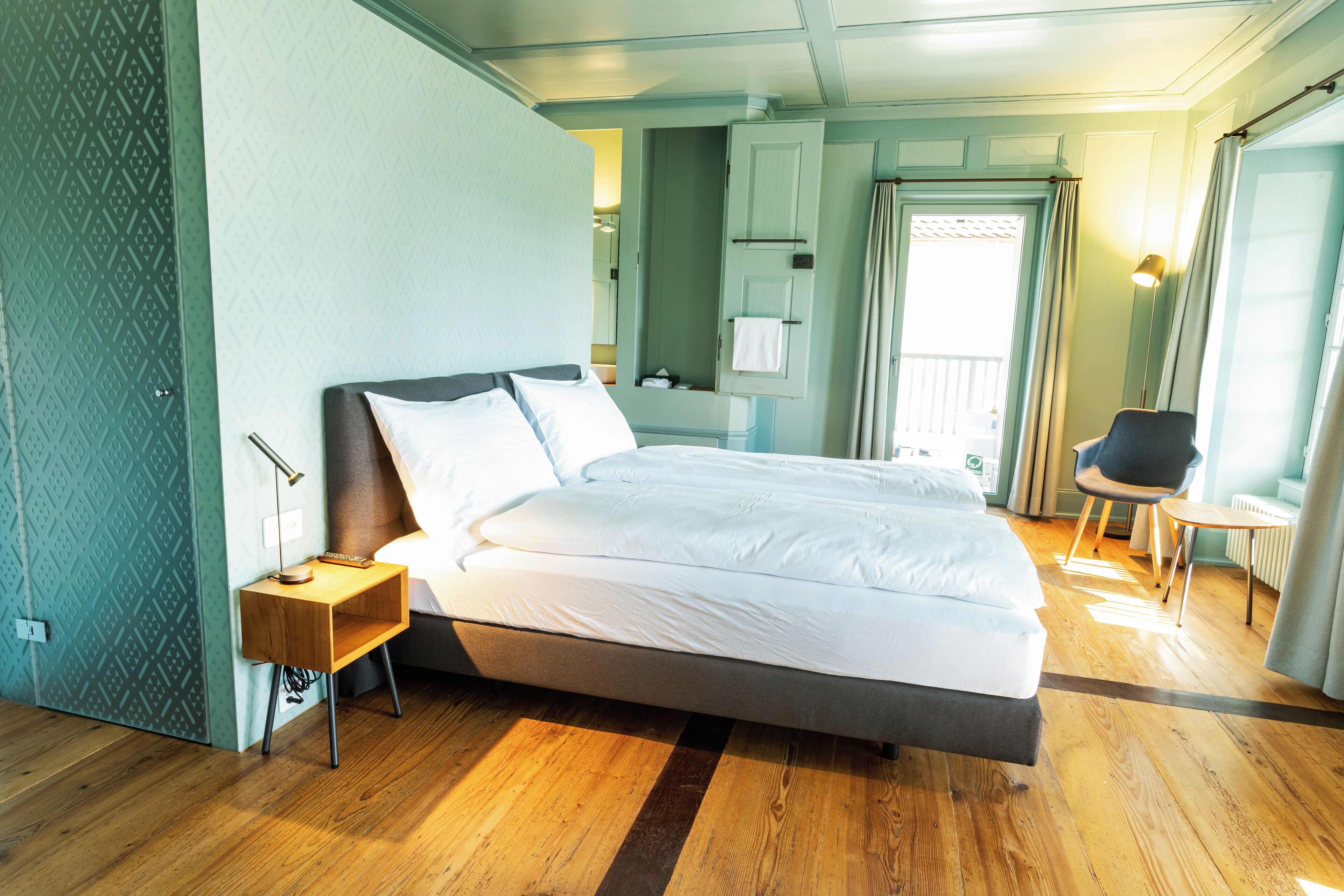 Una habitación de hotel moderna con una cama grande, una mesita de noche, una silla y un vestidor.