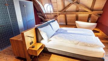A bedroom with a bed, a wooden nightstand, a built-in shelf, a large window, and a wooden ceiling.