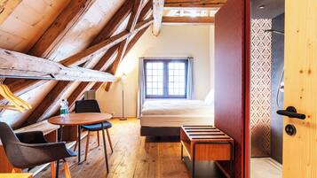 Una habitación con techo inclinado, vigas de madera, cama, ventana, mesa y sillas.