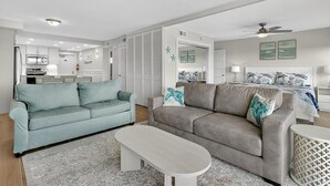 A modern living room with two sofas, a coffee table, and a kitchen in the background. - Gulfstream Condos Unit 504 | Pool, Hot Tub & BBQ Areas | Private Balcony (Corpus Christi)