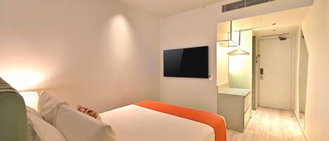 Une chambre d’hôtel moderne équipée d’un lit, d’une télévision à écran plat, d’une table de chevet et d’un dressing.